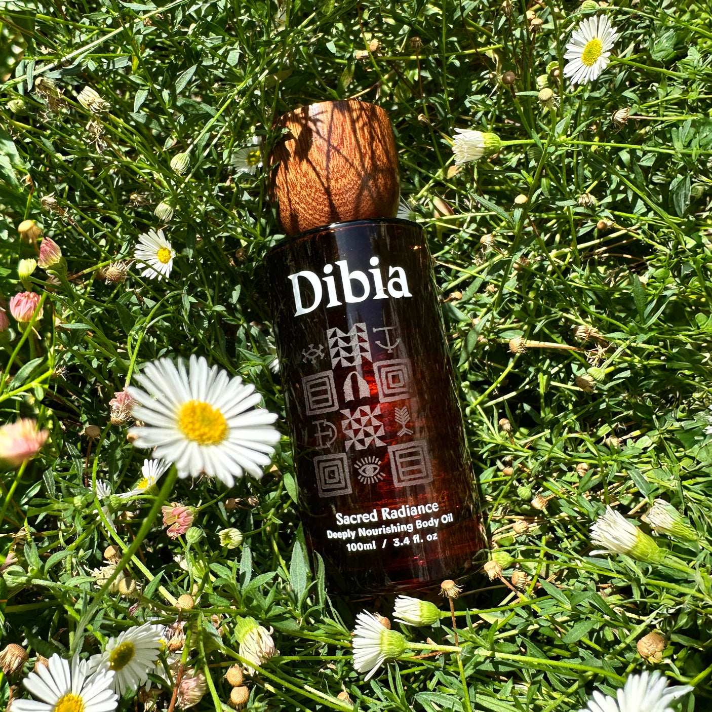 Dibia Sacred Radiance bottle in a field of flowers, sun-kissed lighting warms the scene
